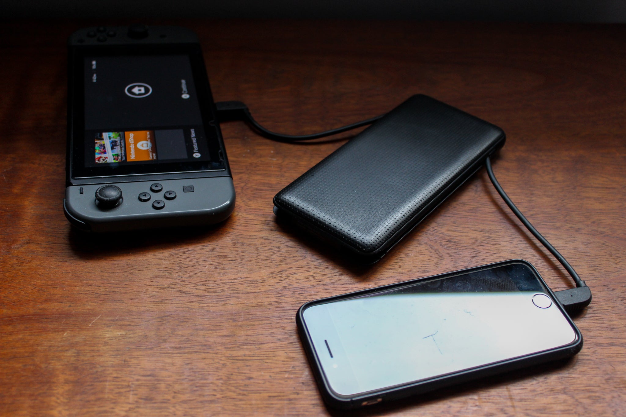 A power bank in the midst of being tested, plugged into a smart phone and a video game to charge both simultaneously.